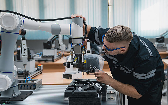 Engineer working on a robotic arm and computer in a tech lab.