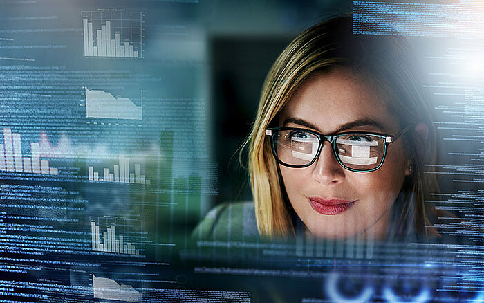 Woman working on a computer surrounded by futuristic holographic charts and graphs, symbolizing financial data analysis, stock trading, and digital transformation.