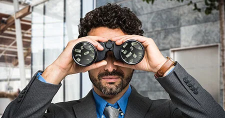 Businessman looking through binoculars with money reflected in the lenses, symbolizing financial foresight or opportunity scanning.