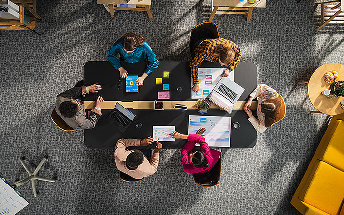 A team of entrepreneurs seated around a conference table, using laptops and tablets to discuss documents and charts.