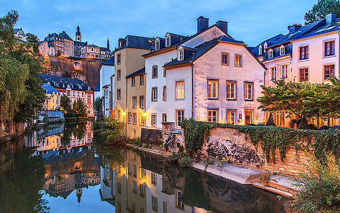 A view of historic buildings in Luxembourg at dusk, softly illuminated by warm streetlights and a fading sky, reflecting European architectural charm.