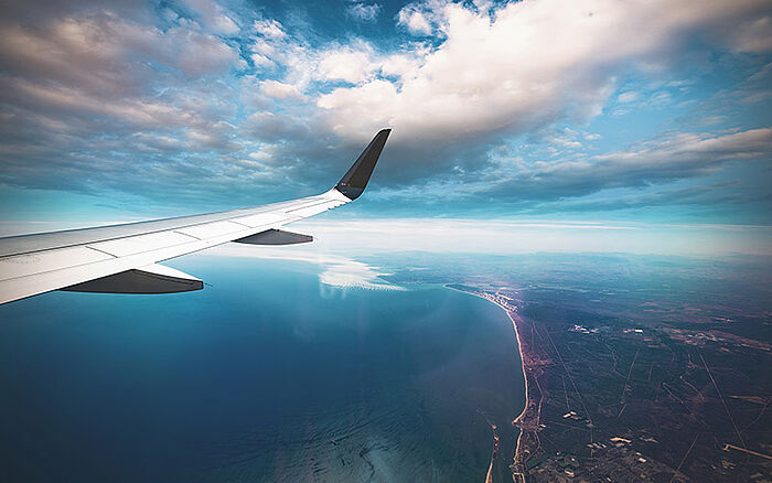 Airplane flying over a city at sunset, viewed from above with dramatic clouds and warm morning light, symbolizing travel, transition and global connection.