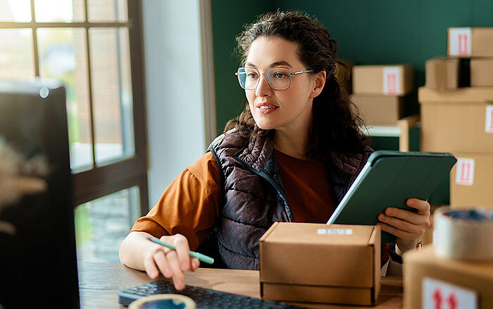 Woman sitting at a computer, taking inventory near shelves stocked with boxes.
