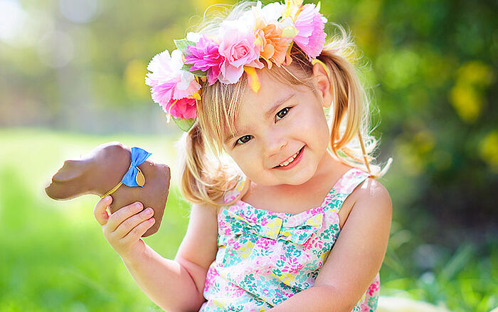 Young girl holding a chocolate Easter bunny, smiling in a bright, festive setting.