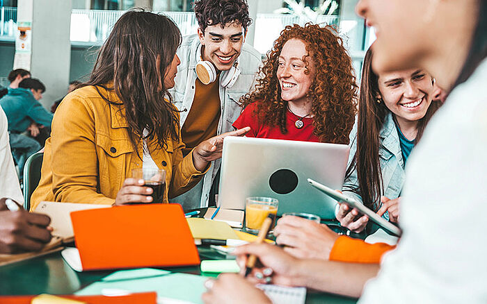 Diverse group of students collaborating with books and a laptop around a study table in a school library.