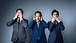 Three businessmen in suits, each covering either their eyes, ears or mouth with their hands, symbolizing the concept of “see no evil, hear no evil, speak no evil” in a corporate setting.