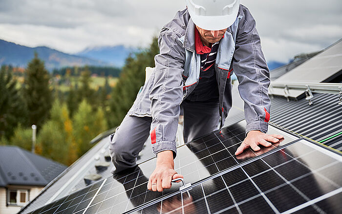 Engineer installing photovoltaic solar panels on a rooftop, using tools to secure a panel, illustrating renewable energy technology and sustainable engineering