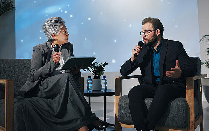 A business panel with speakers on stage discussing market trends and investment strategies at a conference.