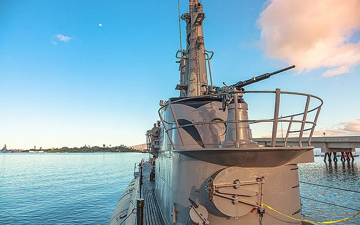 The USS Bowfin submarine docked at Pearl Harbor, serving as a historic World War II memorial under a partly cloudy sky.