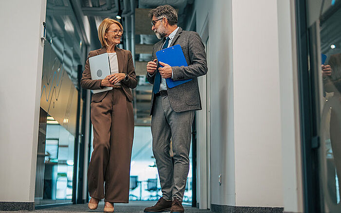 Mature male and female colleagues in business attire discuss a recent agreement.