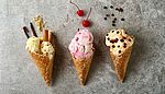 Set of three ice creams of different flavors in waffle cones on grey background