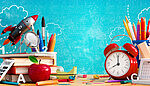Colorful back-to-school themed illustration with a red rocket, pencils, magnifying glass, alarm clock, and calculator against a blue chalkboard background with doodles of clouds and numbers.
