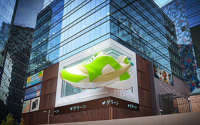 A large 3D digital billboard on the side of a skyscraper in a modern city district showing a giant sneaker as a creative clothing advertisement against the urban skyline and buildings.