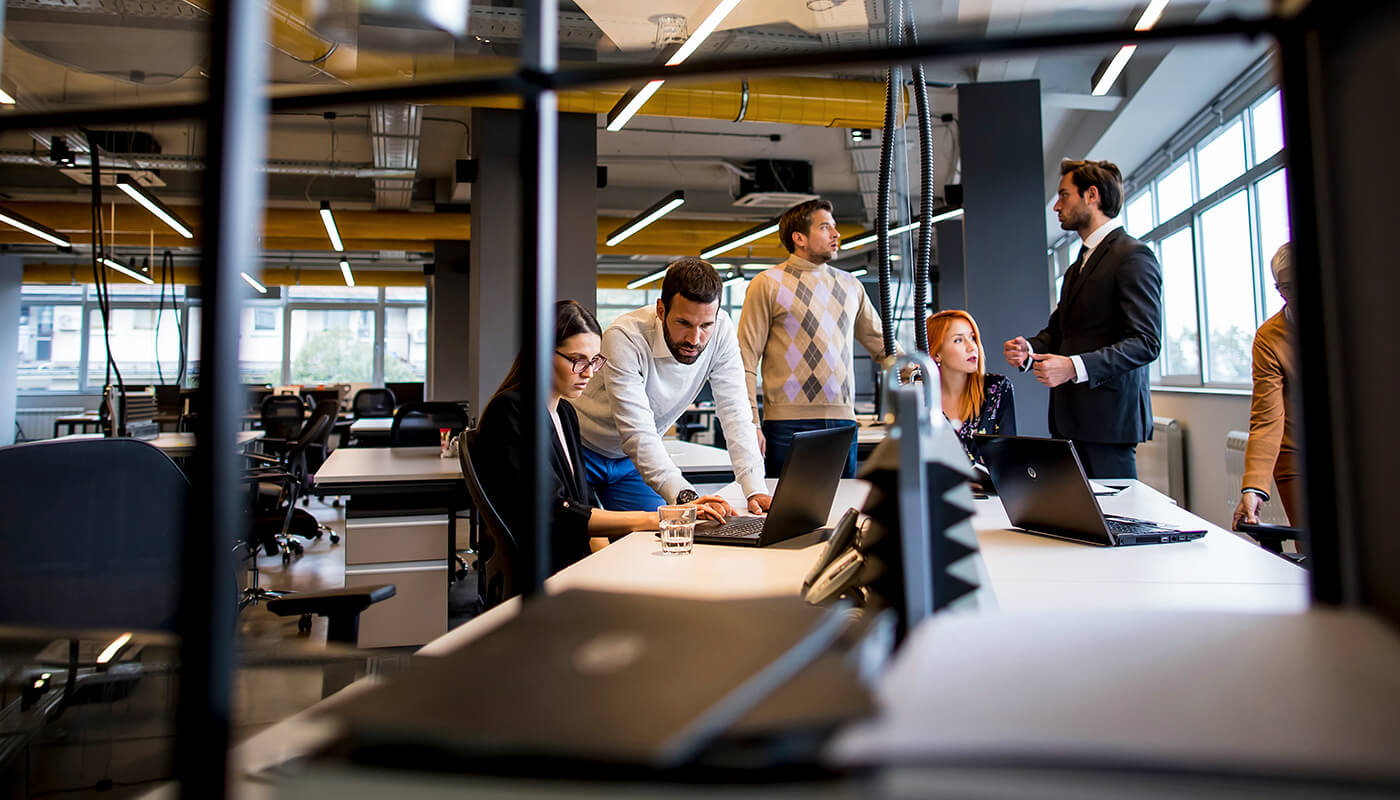 A group of young professionals collaborate in a modern office, with some using laptops and others discussing.