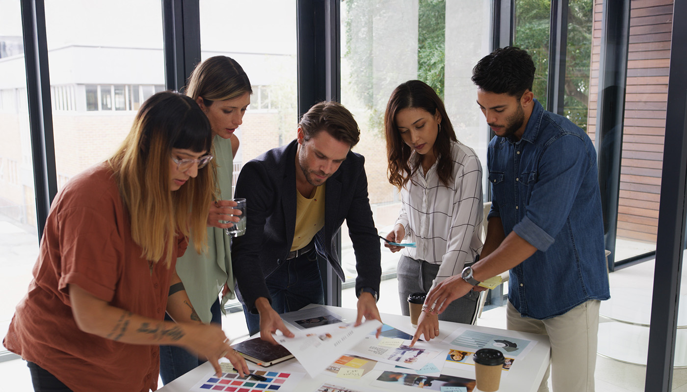 Creative agency staff at a boardroom table holding a colour swatch palette, discussing company branding and design strategy together.